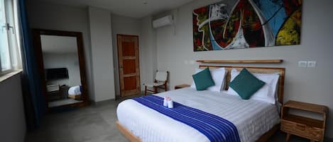 A neatly arranged bedroom with a large bed, a wooden nightstand, a chair, and a colorful abstract painting on the wall.
