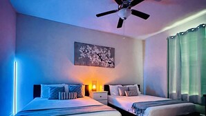 Habitación de hotel con dos camas, un ventilador de techo, un cuadro en la pared y una ventana con cortinas.