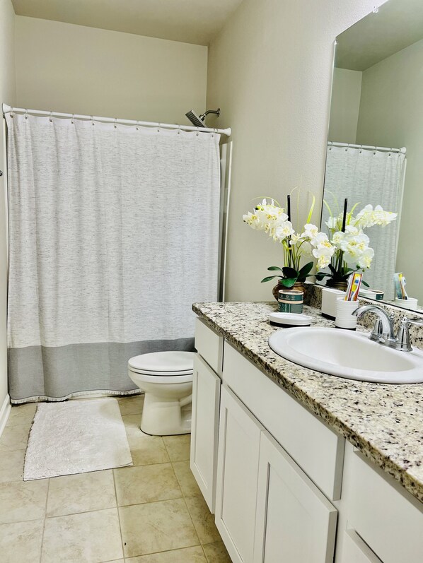 A bathroom with a shower curtain, toilet, sink with a mirror, and a small rug on the floor.