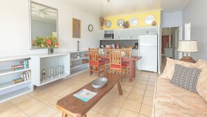 Una sala de estar con una mesa de comedor, sillas, un sofá, una cocina al fondo y un ventilador de techo.