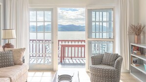 Una habitación con vistas a un lago y montañas, un sofá, una silla y una estantería.