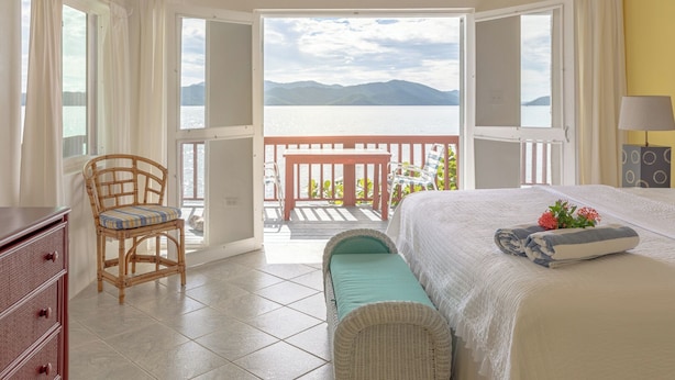 Un dormitorio con cama, una silla, una mesita y vista al mar.