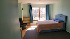 Un dormitorio con una cama, una silla, una ventana con cortinas y vistas a árboles.