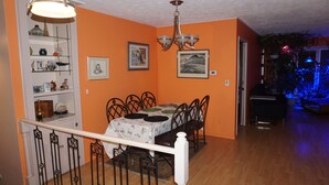 Un comedor con una mesa dispuesta para cuatro personas, rodeada de sillas, en una habitación con paredes anaranjadas y suelo de madera.