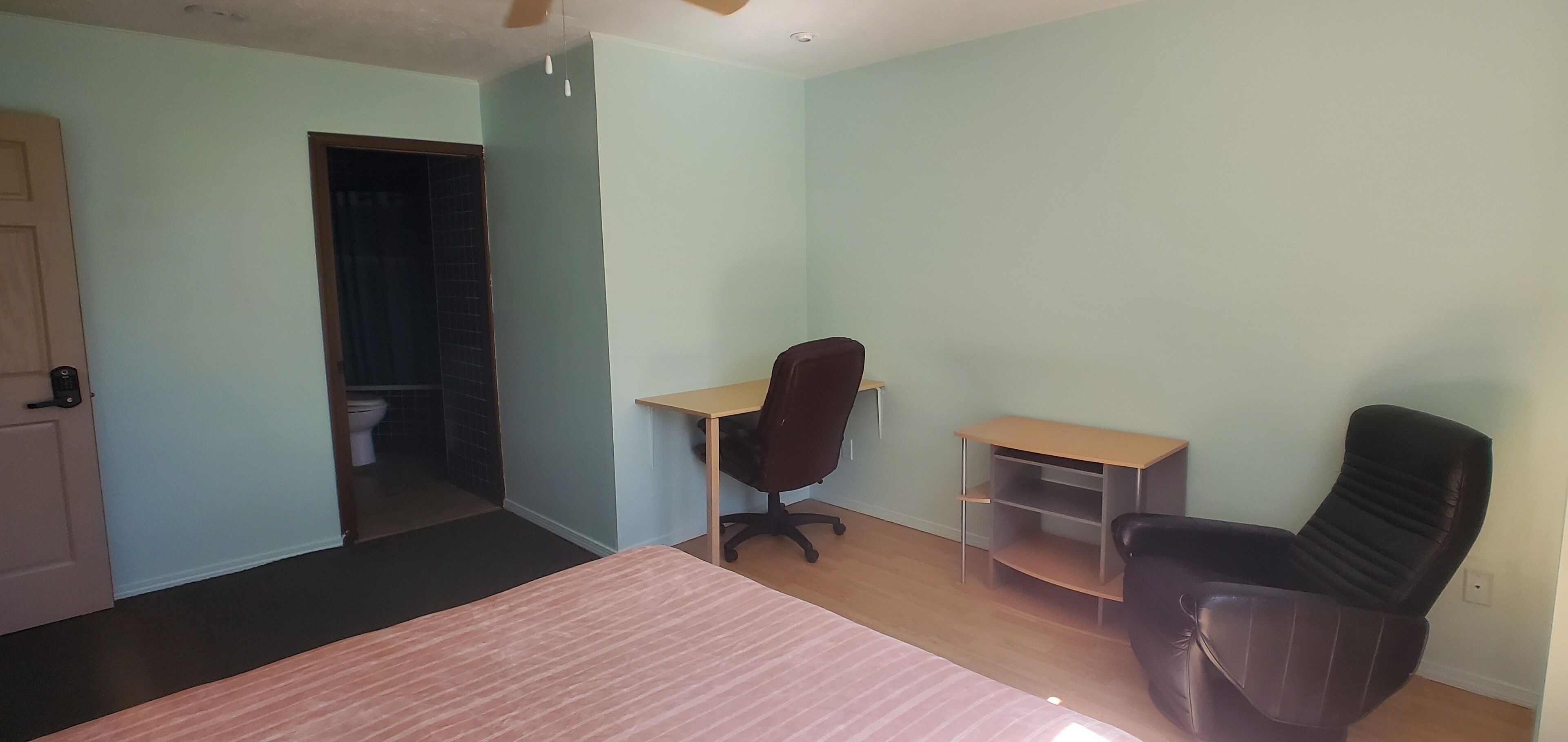 A bedroom with a bed, a desk, a chair, and a door leading to a bathroom.
