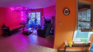 Un salón con sofá, sillones, una mesa de centro y chimenea. Hay plantas en macetas y una ventana con vistas.