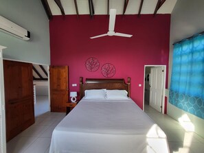 A bedroom with a bed, a ceiling fan, a wooden wardrobe, and a nightstand with a lamp.