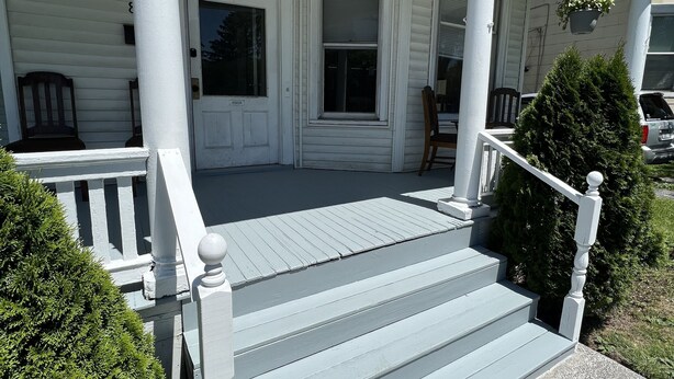 A white house with a front porch, a door, and a window.