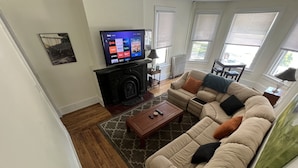 A living room with a fireplace, a sofa set, a coffee table, and a flat-screen TV displaying a streaming service interface.