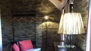 Une pièce chaleureuse avec un mur en pierre, un fauteuil à bascule avec des coussins rouges, une lampe sur pied et un bureau avec une lampe.
