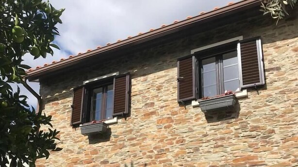 Un bâtiment en pierre doté de deux portes et de fenêtres, d’un petit porche agrémenté d’une plante en pot et d’une boîte aux lettres.