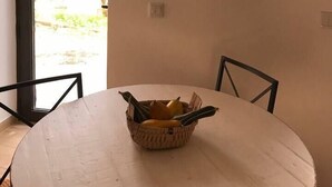 Un coin repas avec une table ronde, un panier de fruits, un luminaire suspendu et une guirlande accrochée au mur.