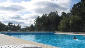 Une piscine à l’eau d’un bleu cristallin, entourée d’arbres et dotée d’une terrasse carrelée.