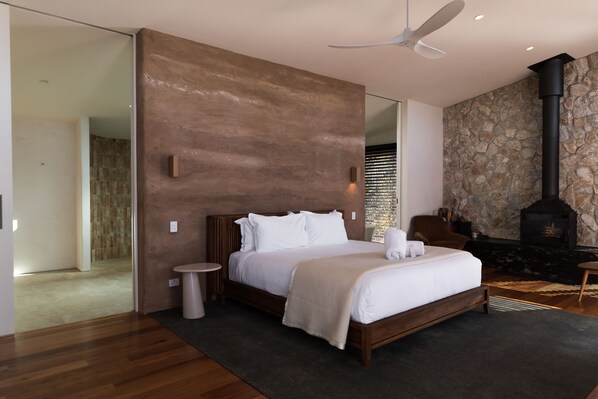 A modern bedroom with a large bed, a stone wall, a fireplace, and a ceiling fan. - Chalets at Blackheath (Blackheath)