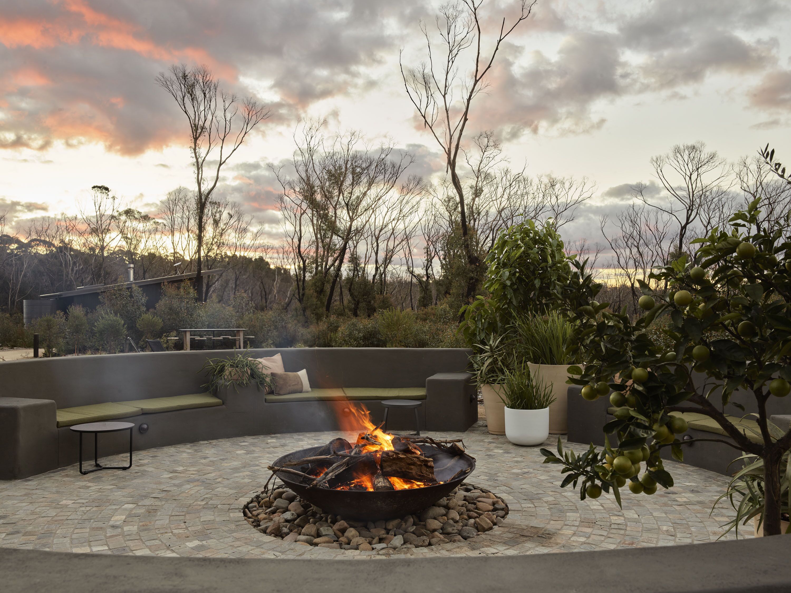 A fire pit surrounded by a stone patio, with outdoor seating and potted plants.