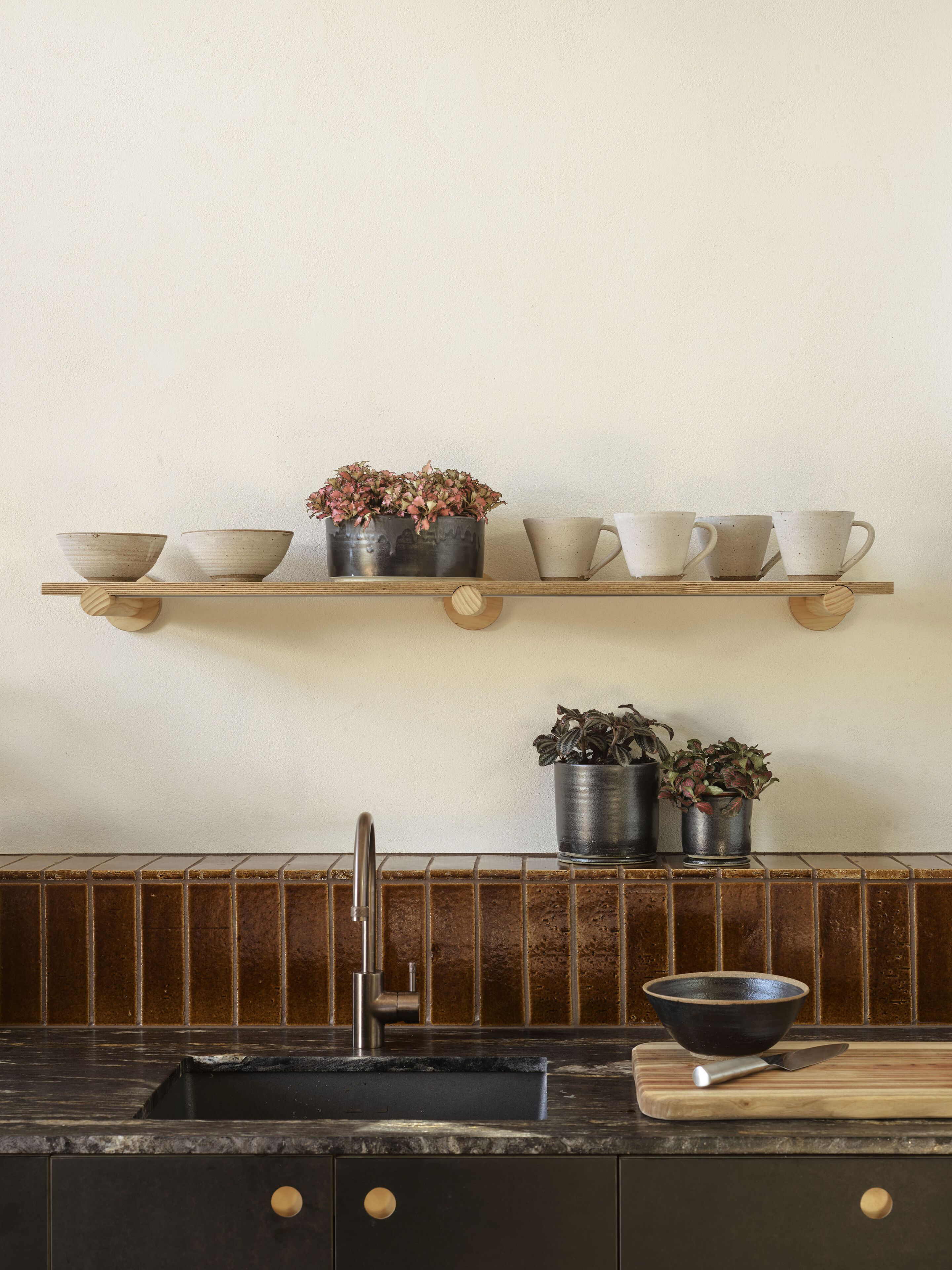 Una cocina con estante de madera que contiene tazones, una planta en maceta y un lavamanos con grifo.