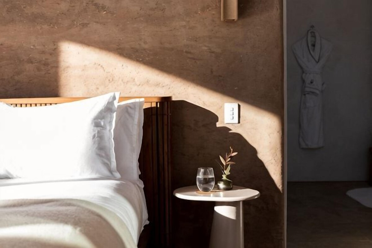 Un dormitorio con cama, mesita de noche con un vaso y una bata colgada en la pared.