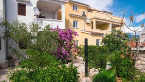 A residential building with a balcony, surrounded by a garden with various plants and a purple flowering bush.