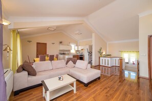 A spacious living area with a large L-shaped sofa, a small white table, and a kitchen in the background.