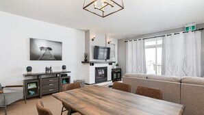 Een moderne woonkamer met een houten eettafel, bank, televisie, open haard en kunst aan de muur.