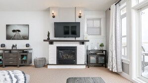 Een moderne woonkamer met een open haard, een flatscreen televisie en een groot raam met gordijnen.