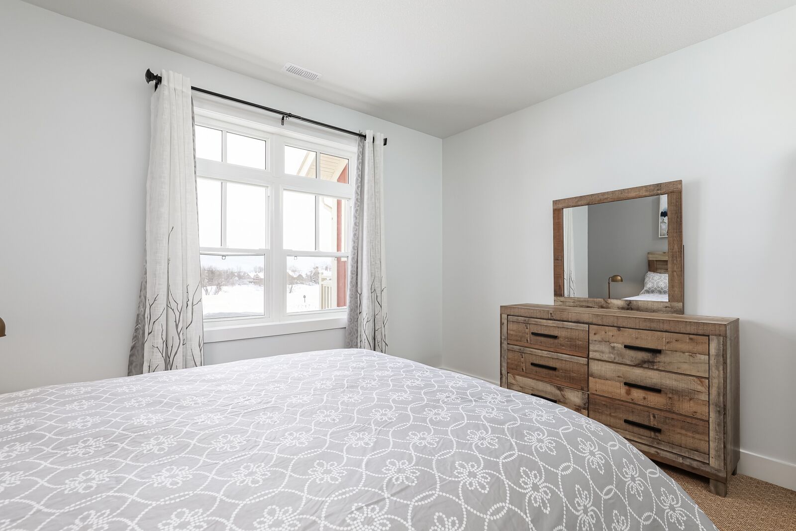 Een slaapkamer met een bed, een kaptafel met spiegel en een raam met gordijnen.