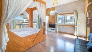 A bedroom with a wooden four-poster bed, a TV, and a balcony with curtains. - Ganghwa Herb Pension (Incheon)