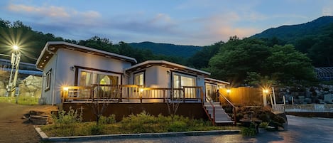 A two-story lodge with a balcony, a wooden deck, and a stone pathway leading to the entrance.