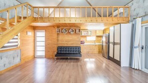A spacious living area with a wooden staircase, a black sofa, and a kitchen with wooden cabinets and a refrigerator. - Ganghwa Herb Pension (Incheon)