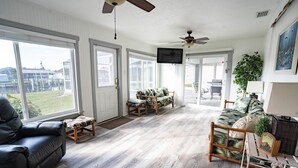 Un salon spacieux avec une grande fenêtre, un ventilateur de plafond et un téléviseur.