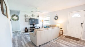 Un salon avec un canapé beige, un plancher en bois, un ventilateur de plafond, un téléviseur et une porte avec une fenêtre.