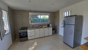 A kitchen with a stove, oven, refrigerator, and a window with blinds. - Cabin in Playa Dorada (Mar chiquita)