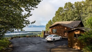 Uma cabana com um carro estacionado em frente, com vista para um lago e montanhas.