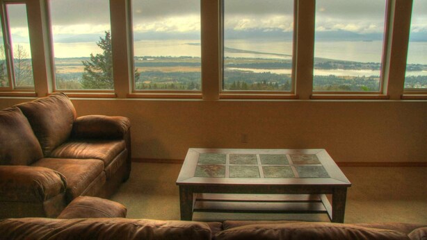 Sala de estar com sofá de couro marrom e uma mesa pequena, janelas amplas com vista para a paisagem.