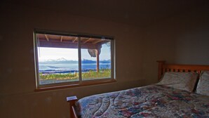 Quarto com cama, janela com vista para montanhas e água, e cabeceira de madeira.