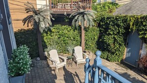 Eine Terrasse mit zwei Adirondack-Stühlen, einem kleinen Tisch und einer Feuerstelle. Im Hintergrund sind Palmen und ein Hecken zu sehen.