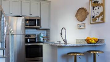 A modern kitchen with stainless steel appliances, a coffee bar, and a staircase leading to an upper level.