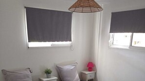 Una habitación con dos camas, una mesita de noche pequeña con lámpara, una ventana con persiana y una lámpara colgante.