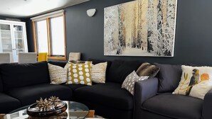 Ein modernes Wohnzimmer mit einem dunkelgrauen Sofa, einem Glastisch und einem gemusterten Teppich.