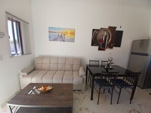 Un salon comprenant un canapé, une table à manger avec des chaises, une table basse avec un saladier, un réfrigérateur et des œuvres d’art accrochées aux murs.