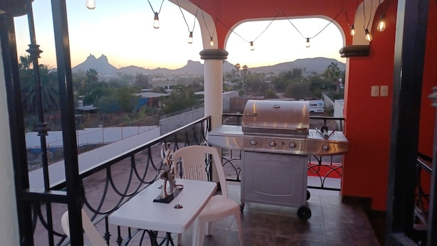 A balcony with a barbecue grill, white chairs, and hanging lights.
