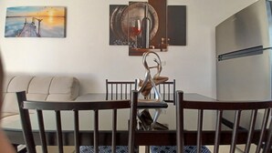 A dining area with a wooden table and chairs, a sofa, and a painting of a sunset.