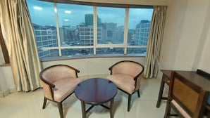 A room with two armchairs and a small table, a large window with a city view, and curtains. - Decale Palace Hotel (Nairobi)