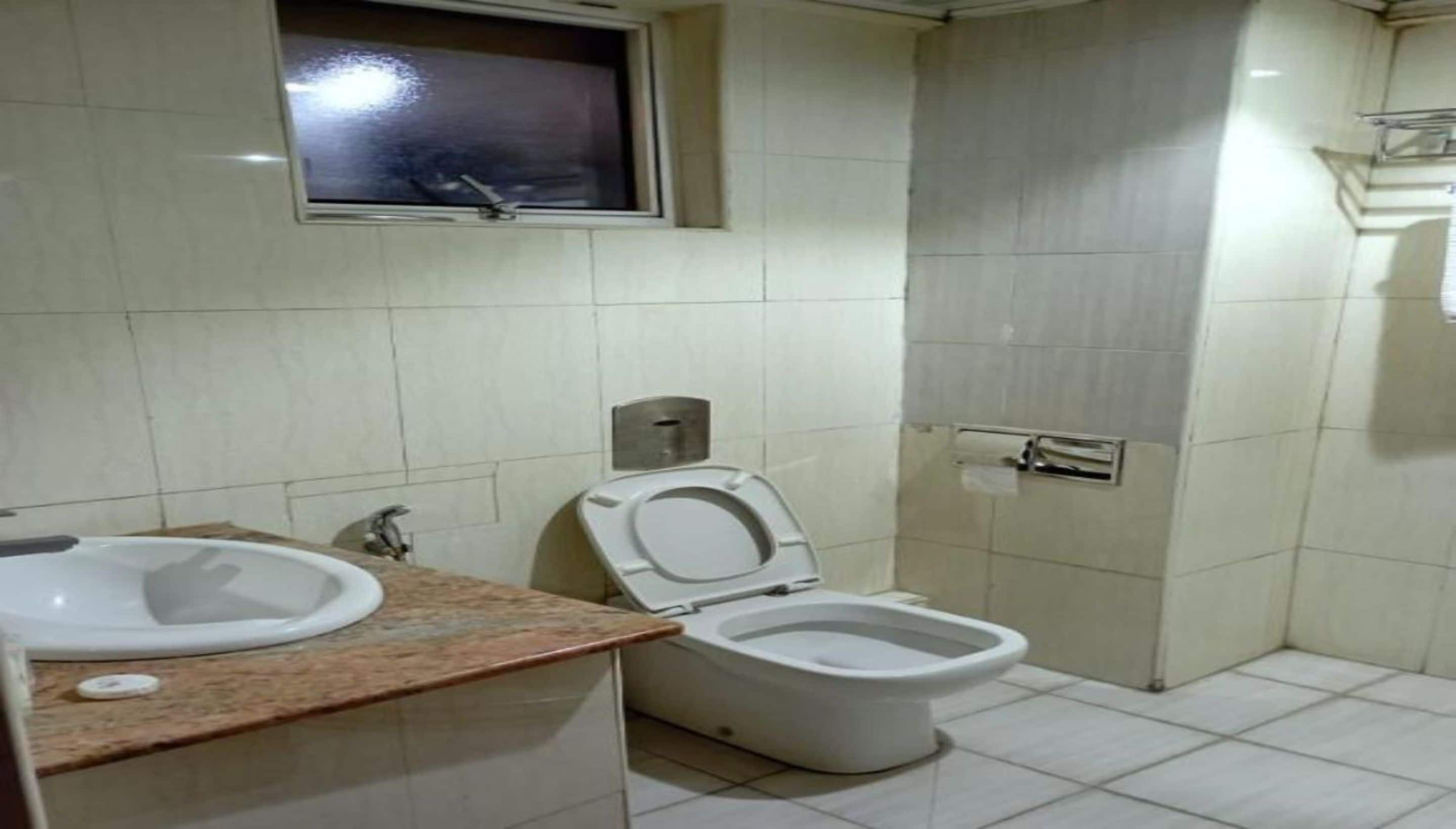 A bathroom with a toilet, sink, and a window above the sink.