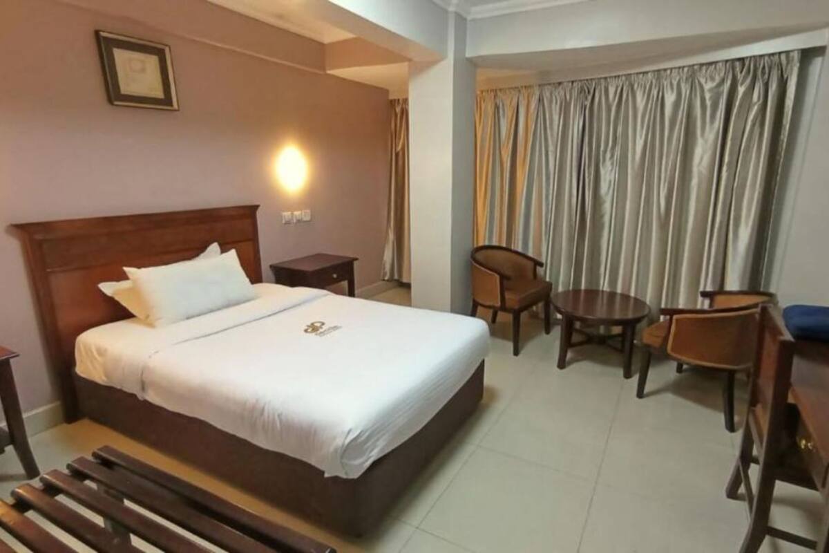 A hotel room with a bed, a desk, a chair, a small table, and a curtain.