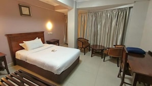 A hotel room with a large bed, a desk, a chair, and a small table. - Decale Palace Hotel (Nairobi)
