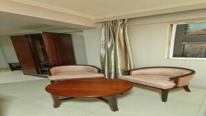 A room with two armchairs and a round wooden coffee table. There is a large mirror on the left and a window with a view of trees. - Decale Palace Hotel (Nairobi)