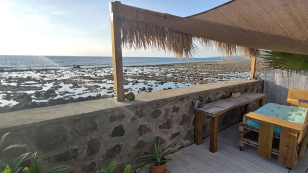 A wooden deck with a table and chairs, overlooking a rocky beach. - Bleu Salé, magnificent waterfront villa (L'Étang-Salé)