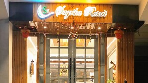 L’entrée d’un restaurant, avec une enseigne au néon, des portes en bois et des plantes en pot.