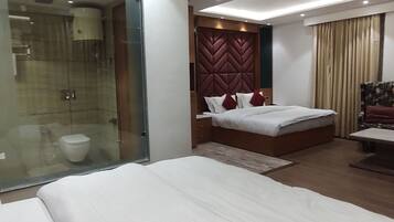 Quarto de hotel moderno com uma cama grande, banheiro separado e uma pequena área de estar.